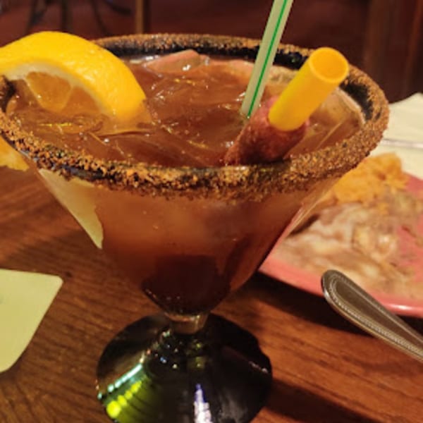 A Mexican michelada cocktail in a salt-rimmed glass with a lemon slice and straw.