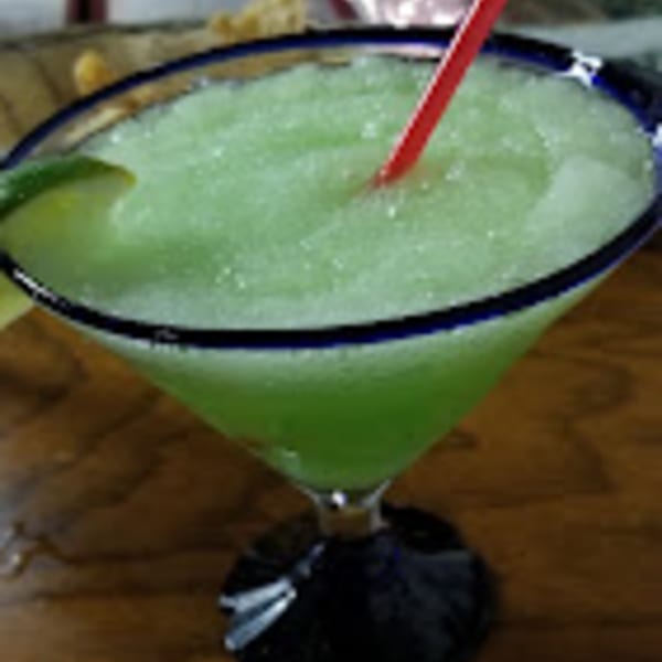 A frozen green margarita with a red straw and lime wedge in a blue-rimmed glass.