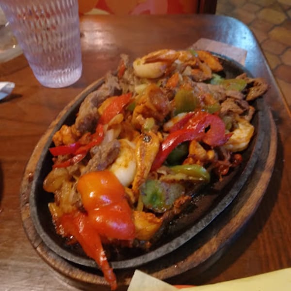 Sizzling fajitas with steak, shrimp, red and green bell peppers, and onions on a wooden platter.