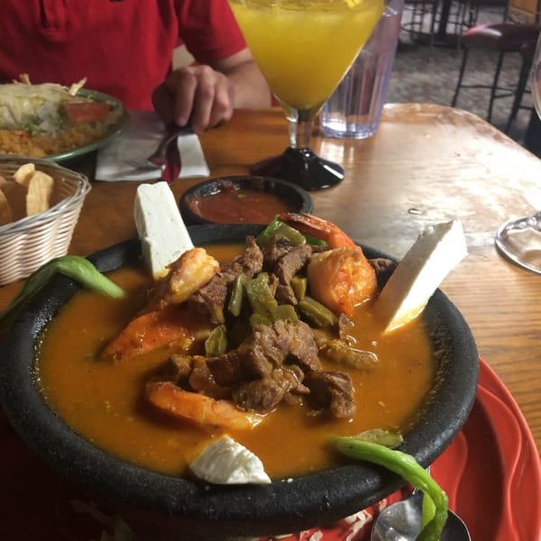 Molcajete with beef, shrimp, and cheese, with a person eating in the background at Macarios Grill.