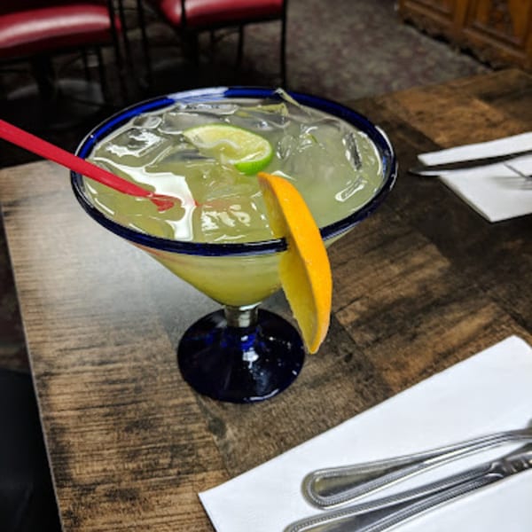 A Macarios Grill margarita in a blue-rimmed glass with lime, orange, and a red straw.